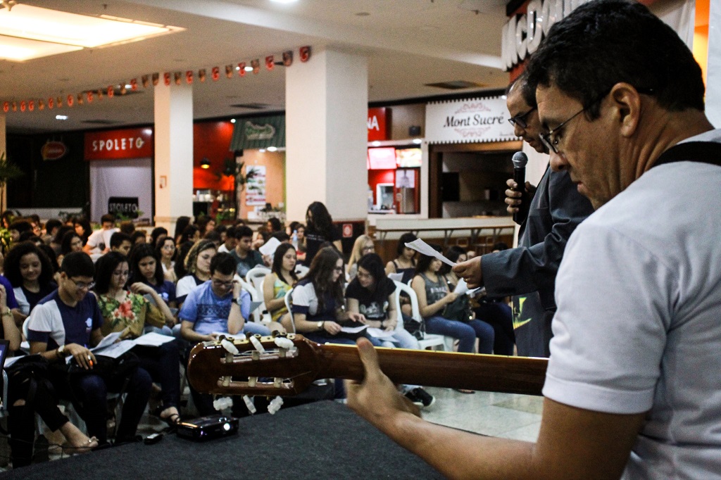 professor tocando violão para alunos em praça de alimentação de shopping