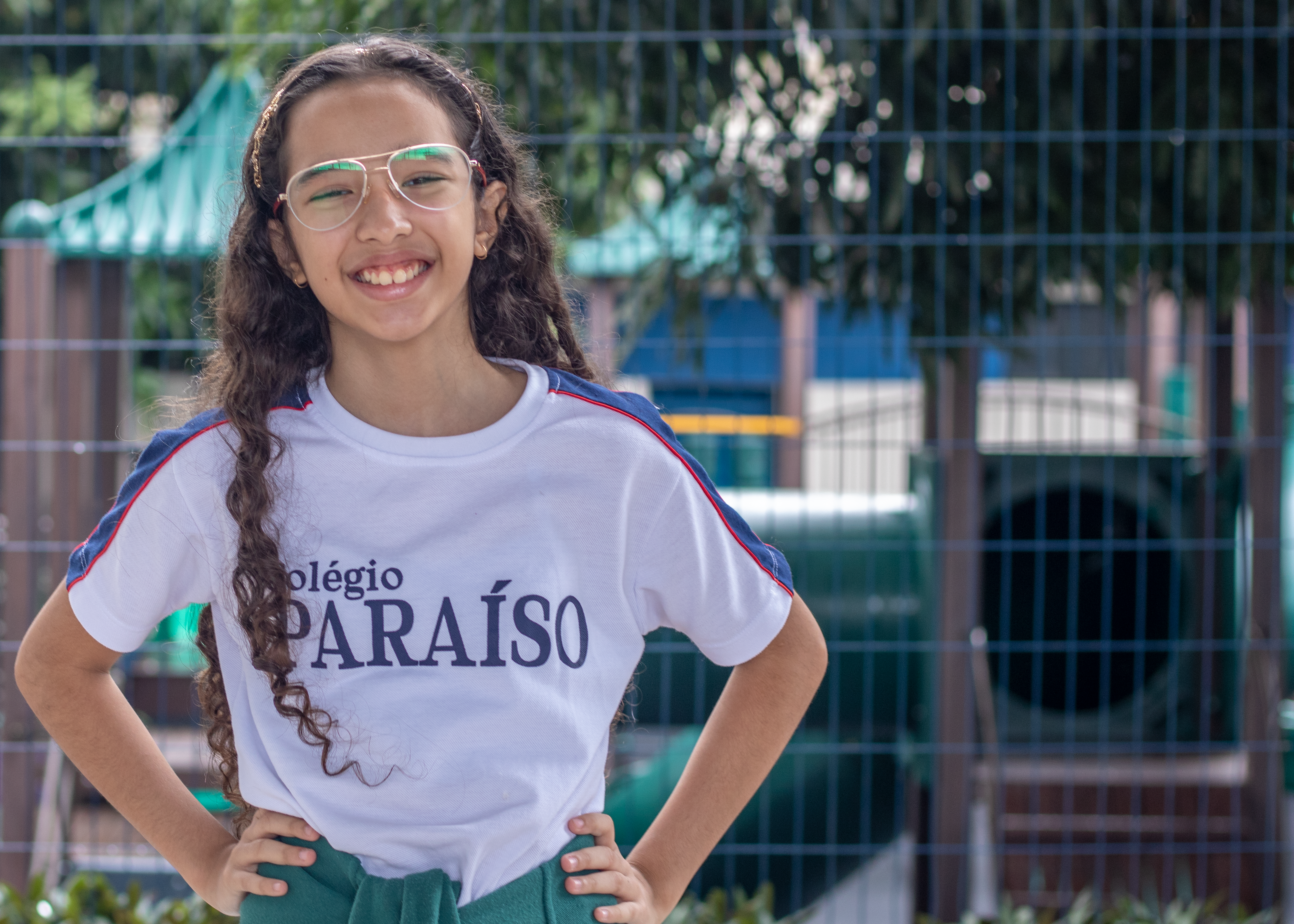 aluna do colégio paraíso sorrindo e pátio com brinquedos ao fundo