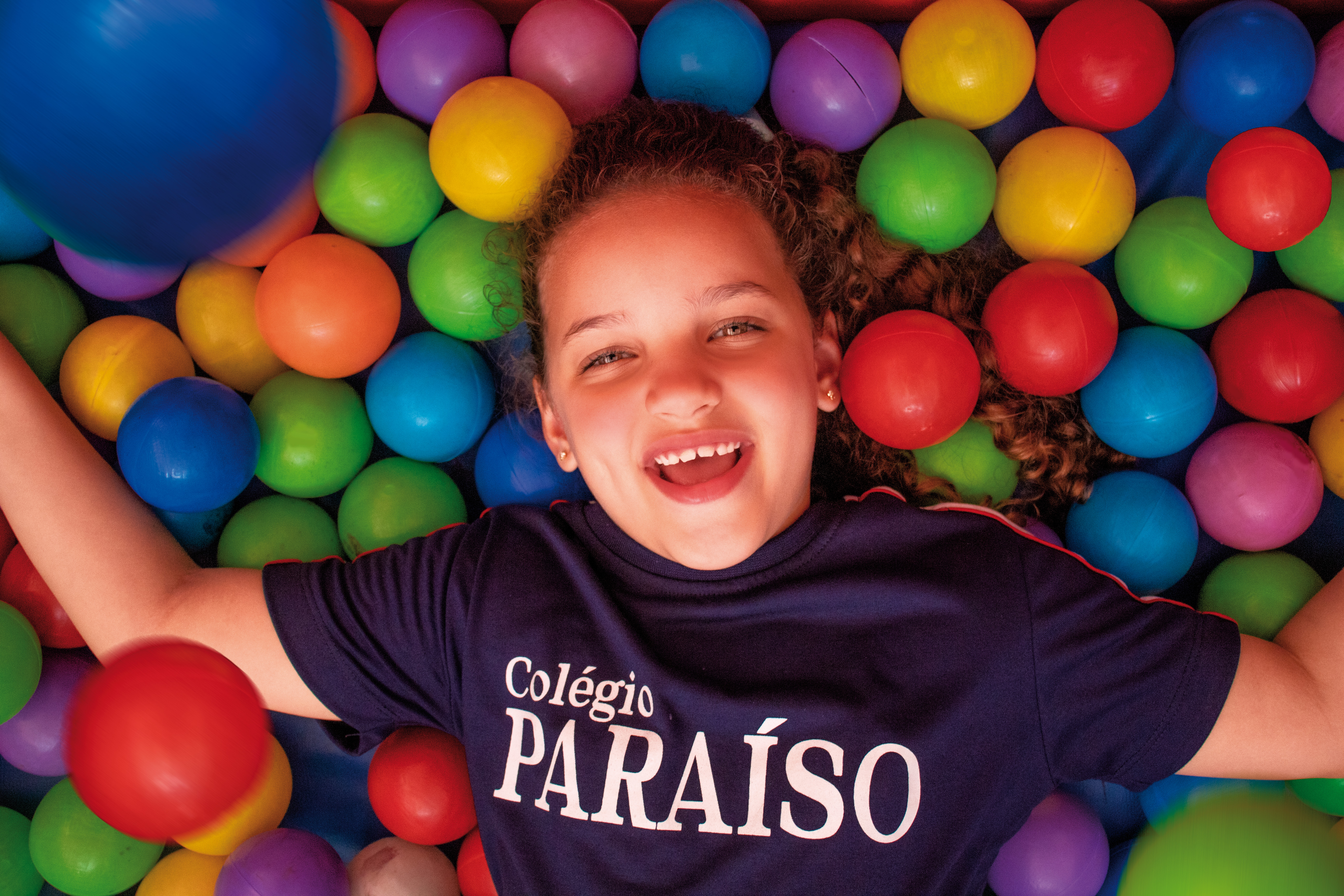 aluna sorrindo deitada em piscina de bolinhas coloridas